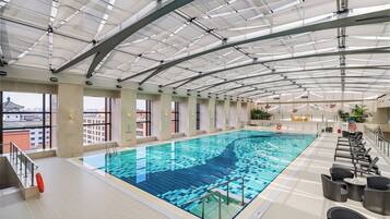 An indoor swimming pool with clear glass ceilings, a lifeguard chair, and a poolside seating area.