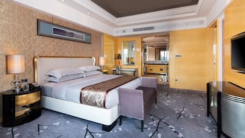 A hotel room with a large bed, bedside tables, a desk, a chair, a TV, and a bathroom visible through an open door.