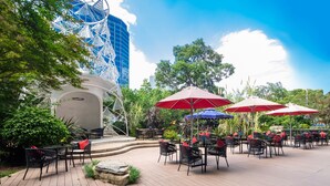 An outdoor patio with tables and chairs, surrounded by greenery and a modern building with a unique design. - Wyndham Grand Plaza Royale Colorful Yunnan Kunming (Kunming)