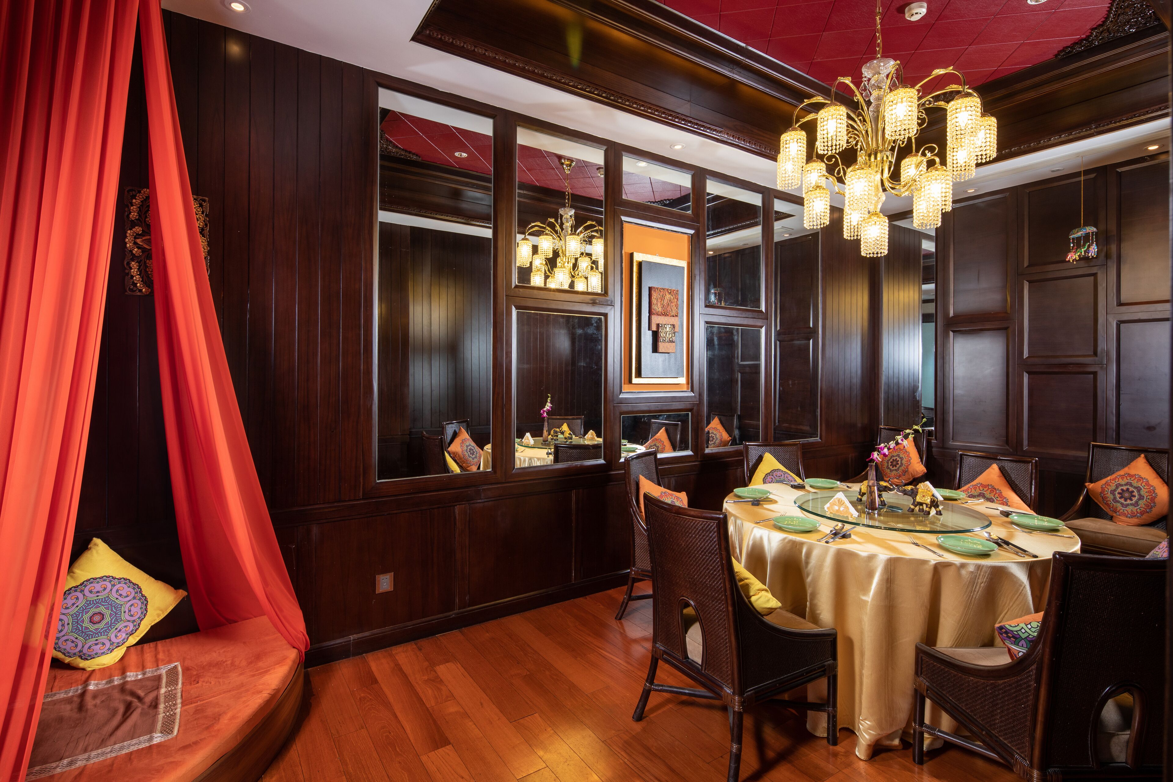 A dining area with a round table set for four, surrounded by wicker chairs, a red canopy, and a chandelier.