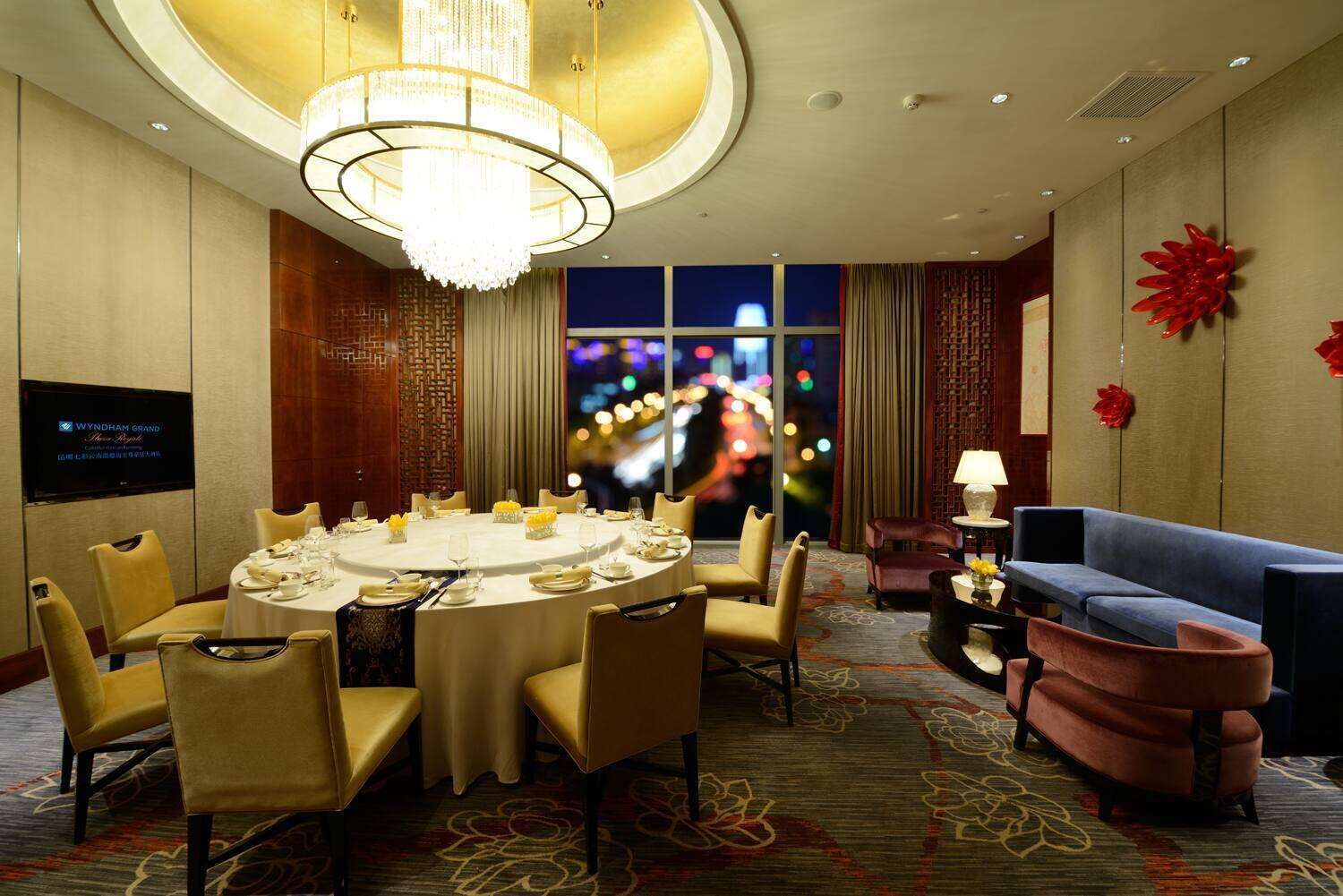 A hotel room with a round dining table set for six, a sofa, and a TV mounted on the wall.