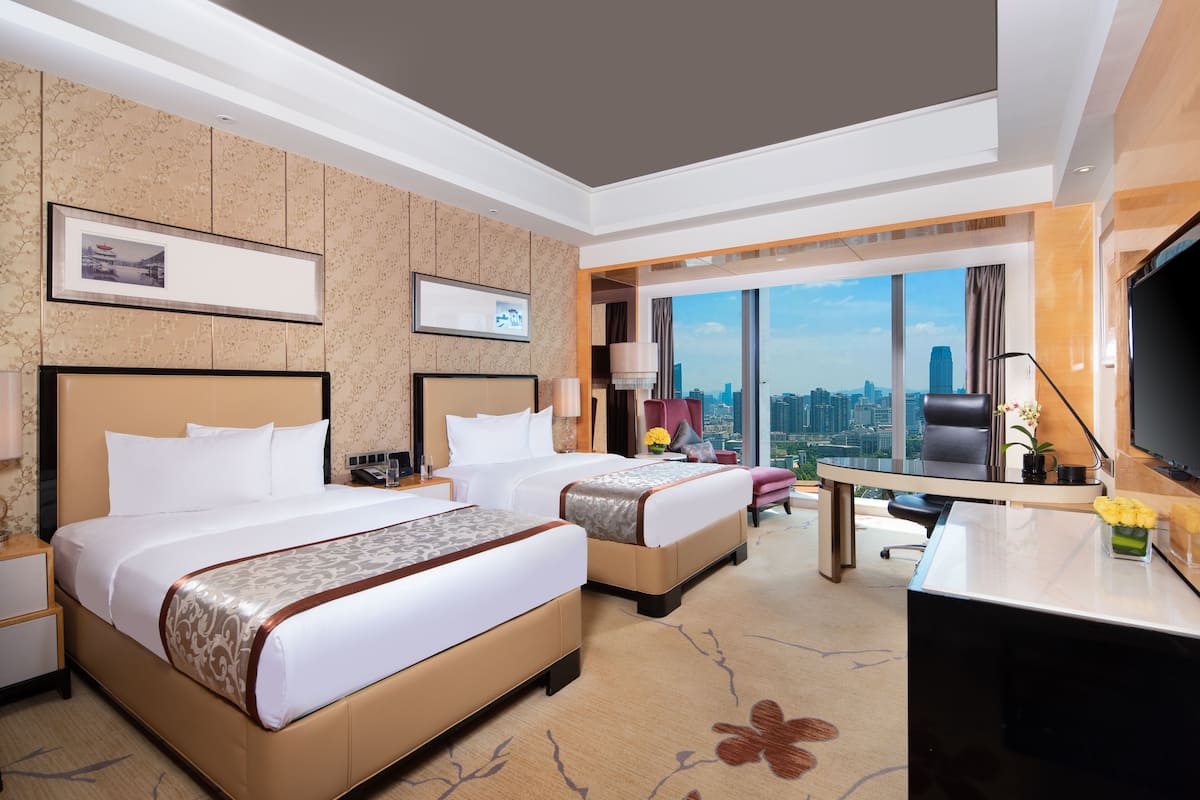 Une chambre d’hôtel avec deux lits, un bureau et une grande fenêtre donnant sur la ville.