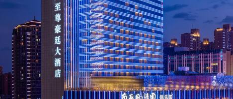 Un hotel de varios pisos con señalización iluminada, una entrada destacada y vistas de la ciudad circundante.