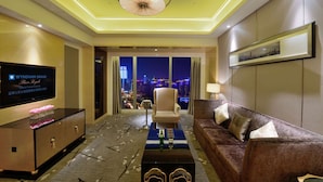 A hotel room with a large TV, a sofa, a coffee table, and a view of the cityscape at night. - Wyndham Grand Plaza Royale Colorful Yunnan Kunming (Kunming)