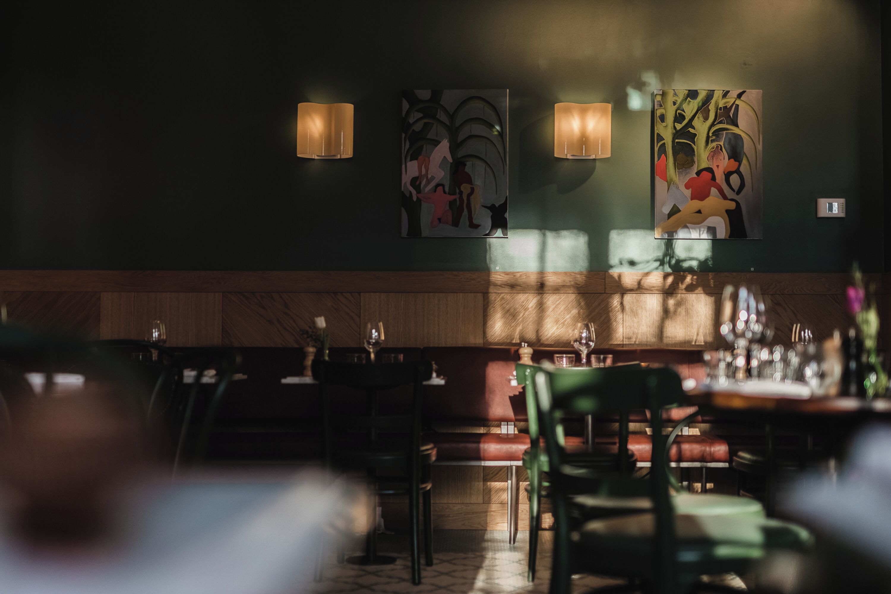 A dimly lit restaurant interior with wooden paneling and modern art on the walls.