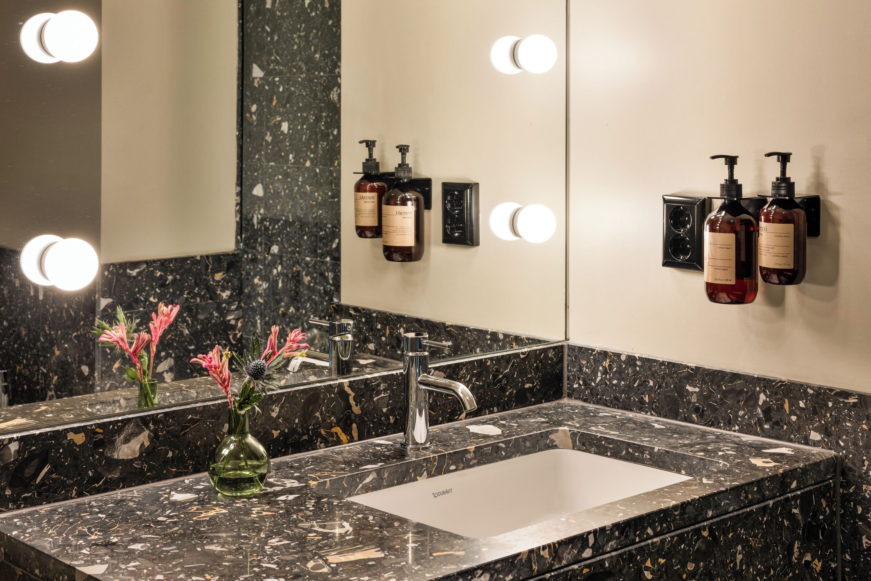 A bathroom with a marble sink, a mirror, and two bottles of shampoo.