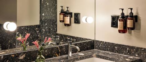 A bathroom with a marble sink, a mirror, and two bottles of shampoo.