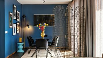 A modern living room with a blue wall, a black sofa, a dining table with chairs, and a decorative vase with flowers.