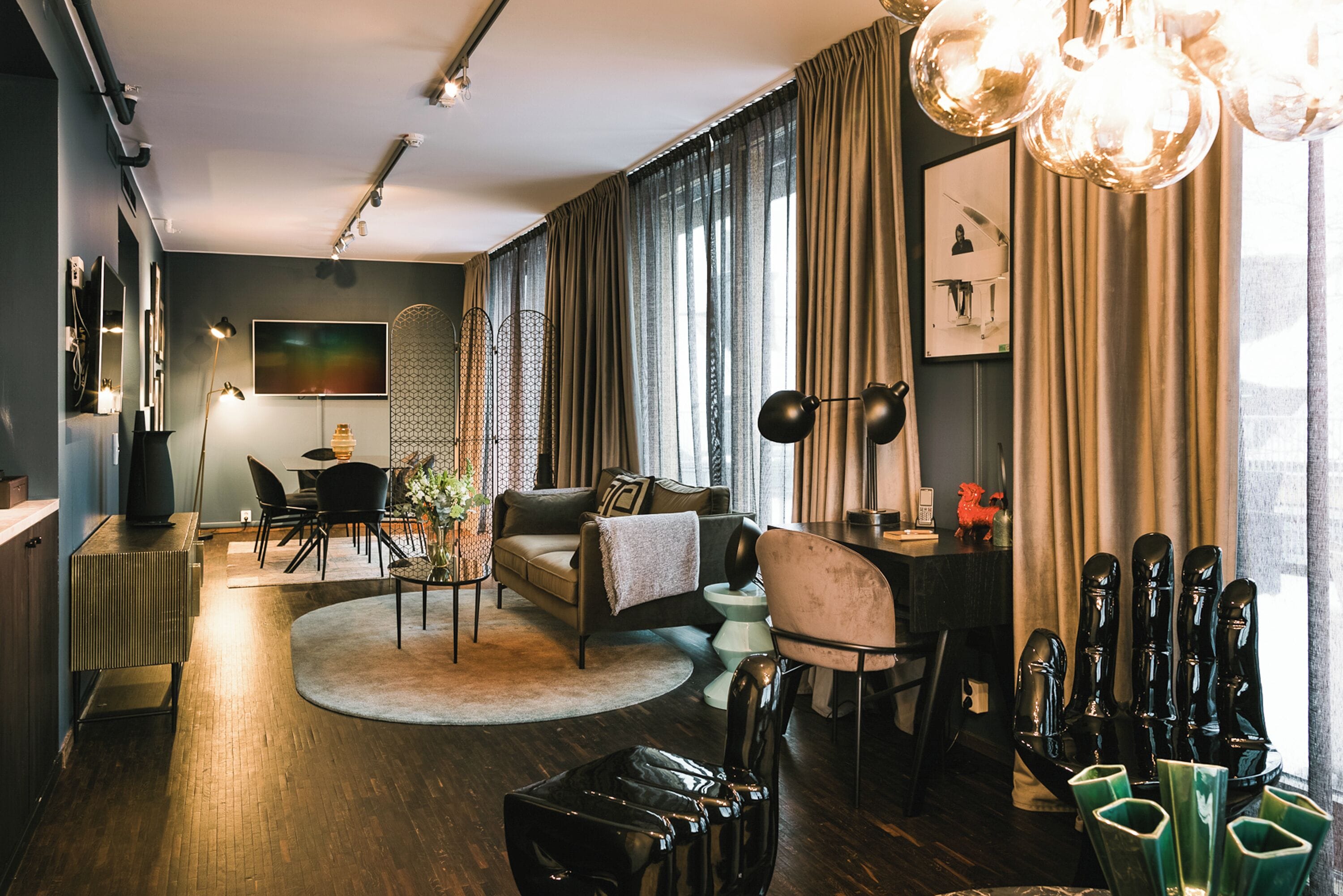 A modern living room with a sofa, coffee table, and chairs. There is a television, a lamp, and a window with curtains.