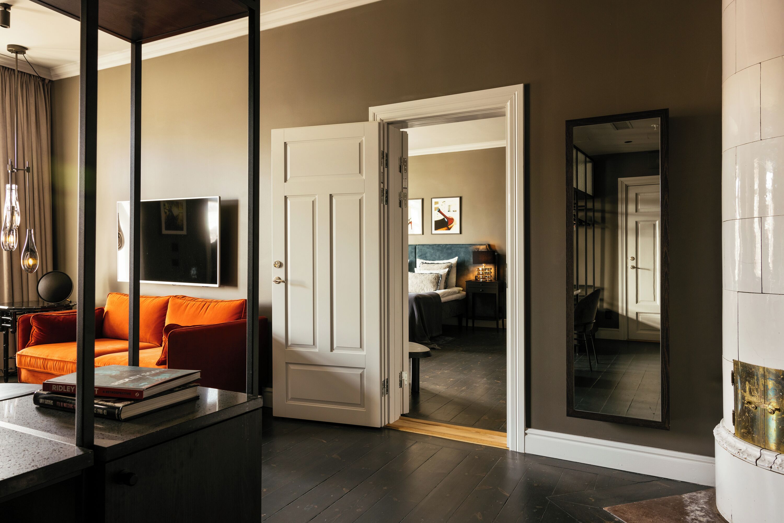 A modern living room with a dark wood floor, a white door leading to another room, and a large mirror reflecting the room.