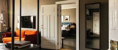 A modern living room with a dark wood floor, a white door leading to another room, and a large mirror reflecting the room.