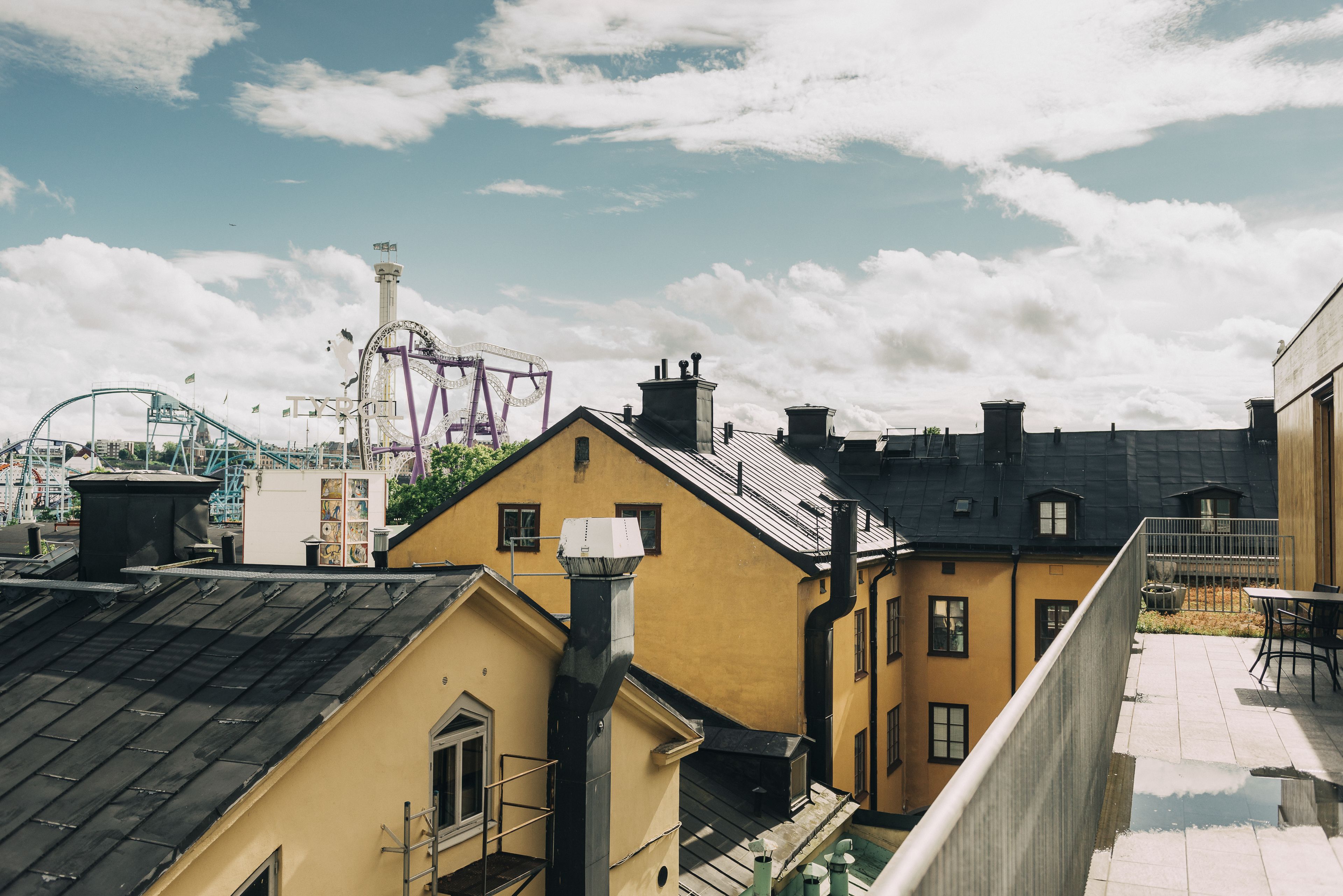 Udsigt til en bygning med gul facade, sort tag og en balkon med et bord og stole.