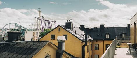 Udsigt til en bygning med gul facade, sort tag og en balkon med et bord og stole.