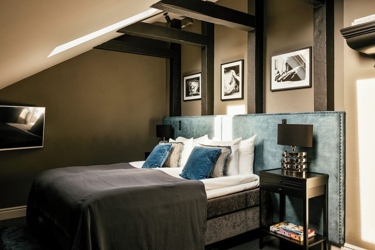 A bedroom with a bed, pillows, a bedside table with a lamp, and framed pictures on the wall.