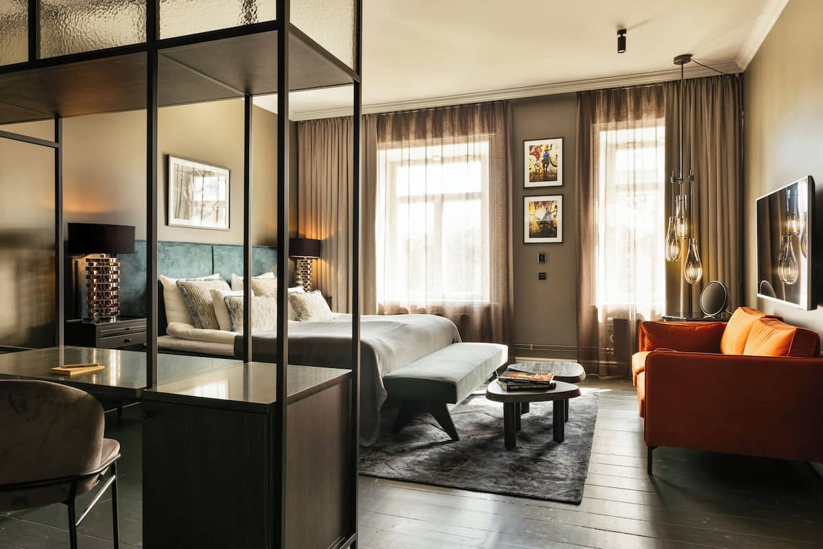 A modern hotel room with a bed, a sofa, a desk, and a dining table.