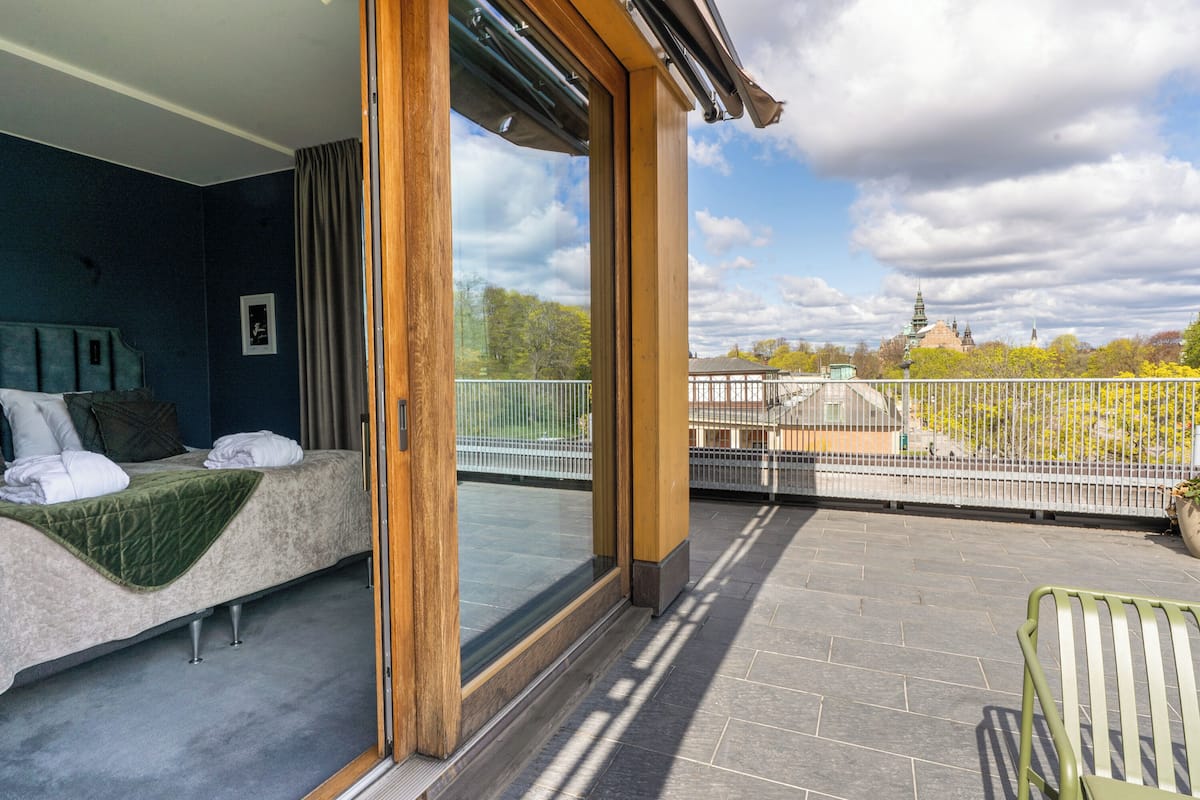 A balcony with a bed, a view of a cityscape, and a railing.