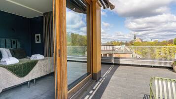 A balcony with a bed, a view of a cityscape, and a railing.