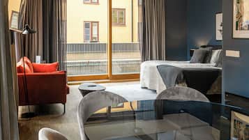 Habitación de hotel con cama, un sillón rojo, una mesa de vidrio y vista al balcón exterior.