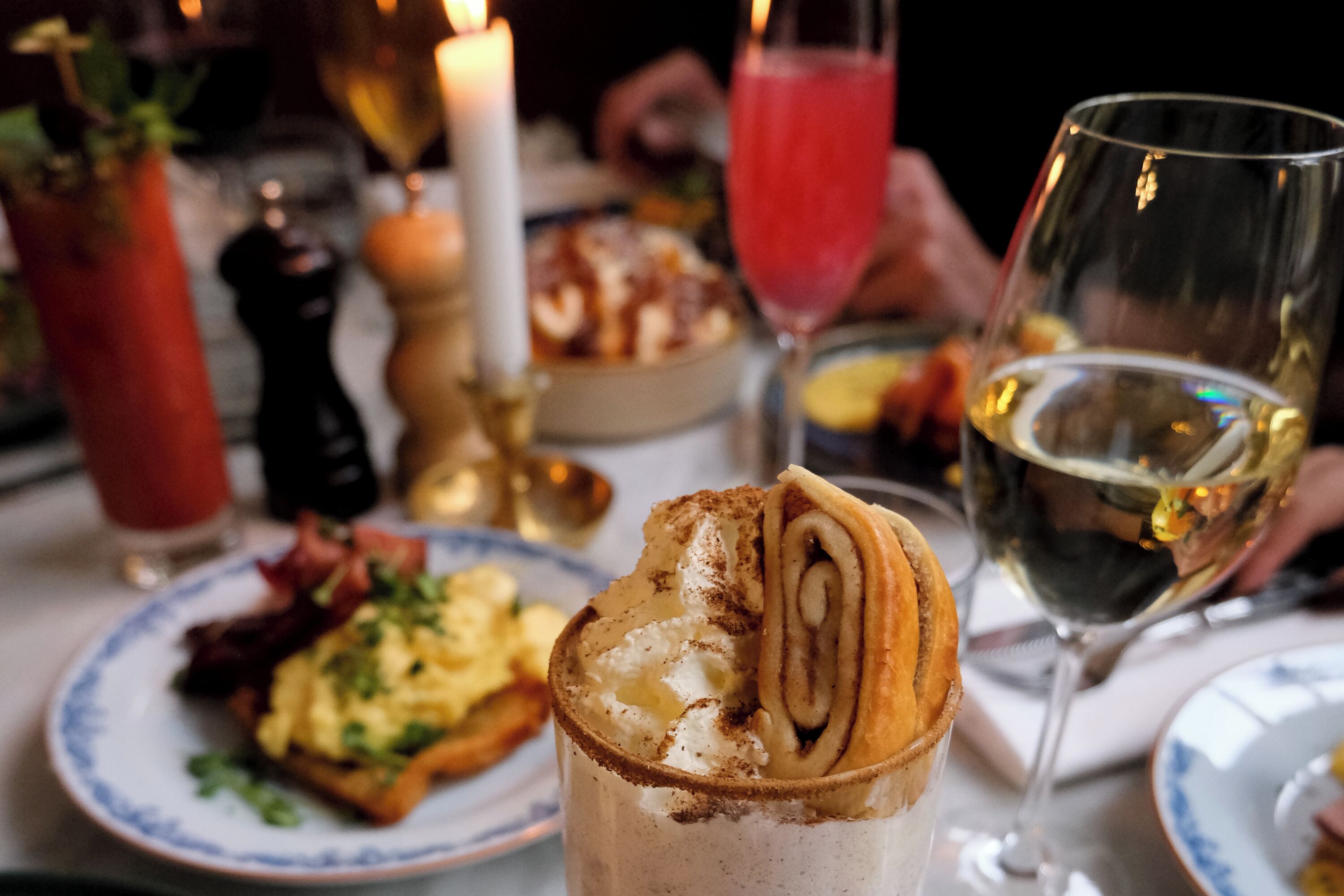 Una mesa de comedor con un postre, una copa de vino blanco y una vela.