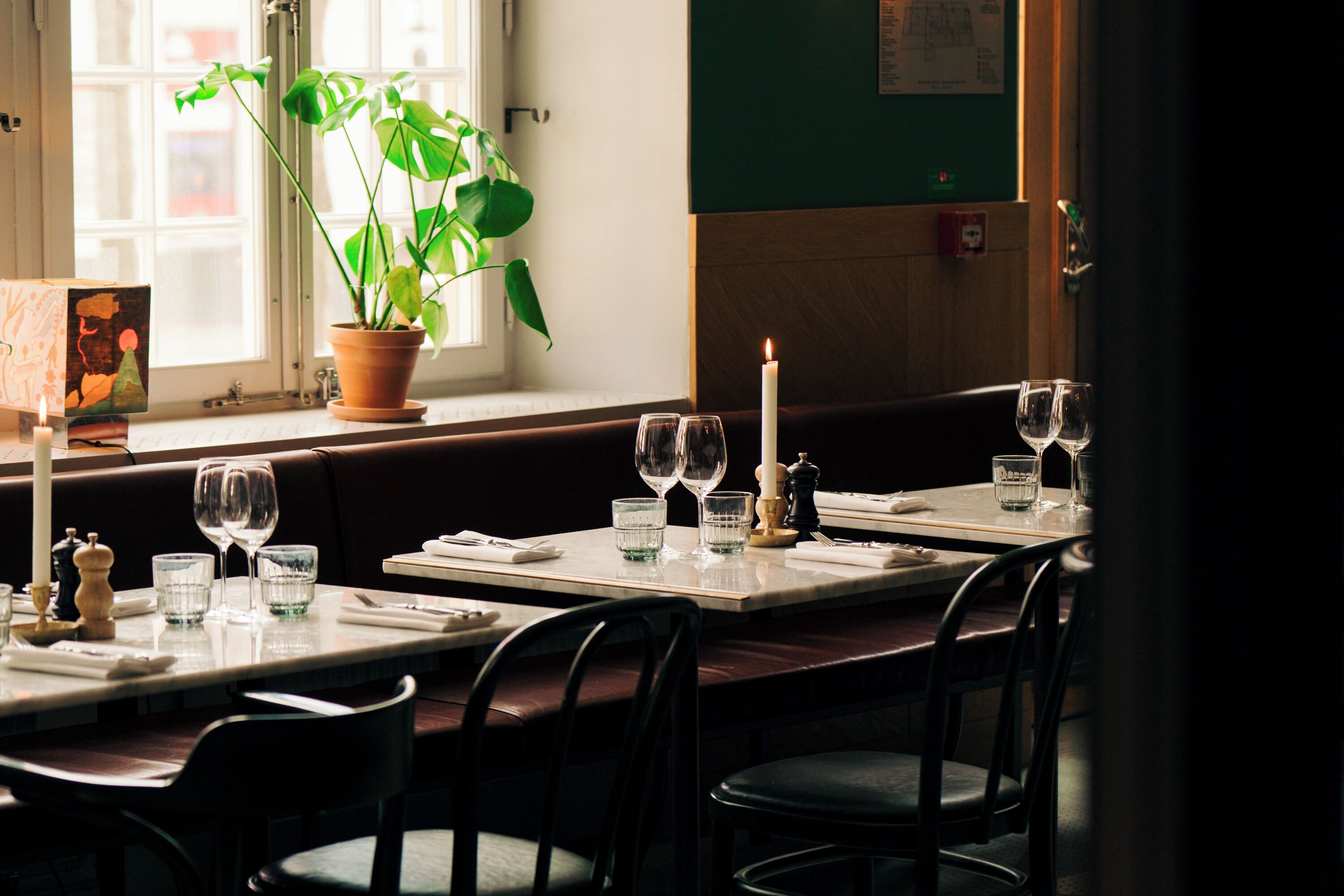 Un restaurant avec des tables dressées, une plante en pot et une bougie sur la table.