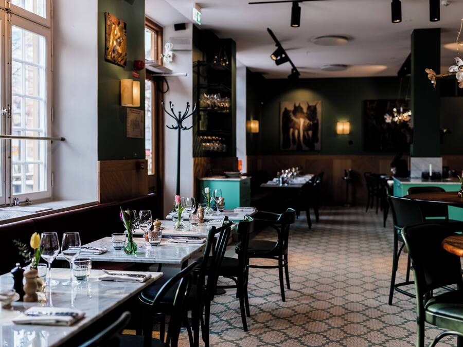 Interior de restaurante con mesas dispuestas para comer, piso estampado y vista a través de amplios ventanales.