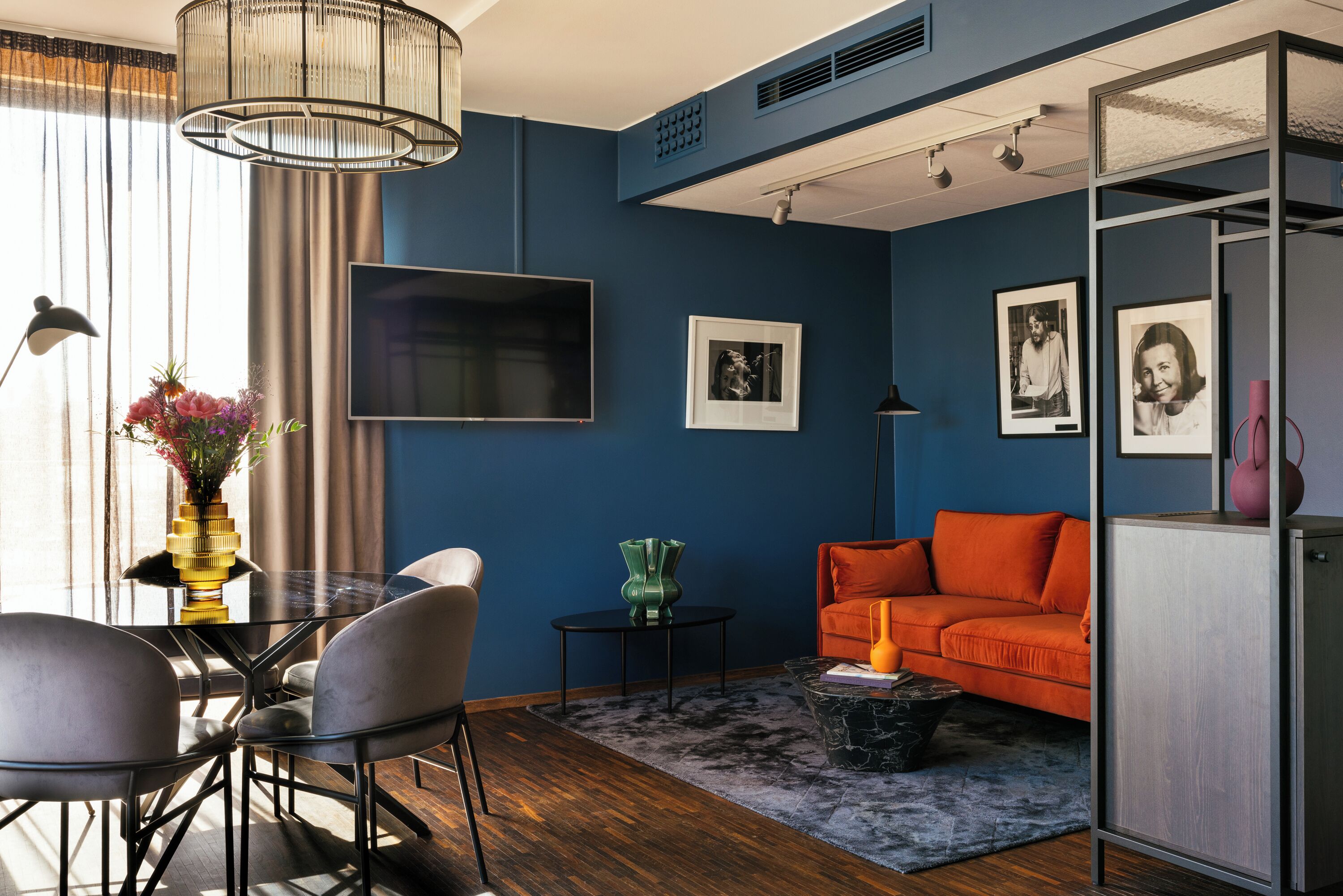 Una sala moderna con una pared azul de acento, un sofá, una mesa de comedor con sillas y un televisor.