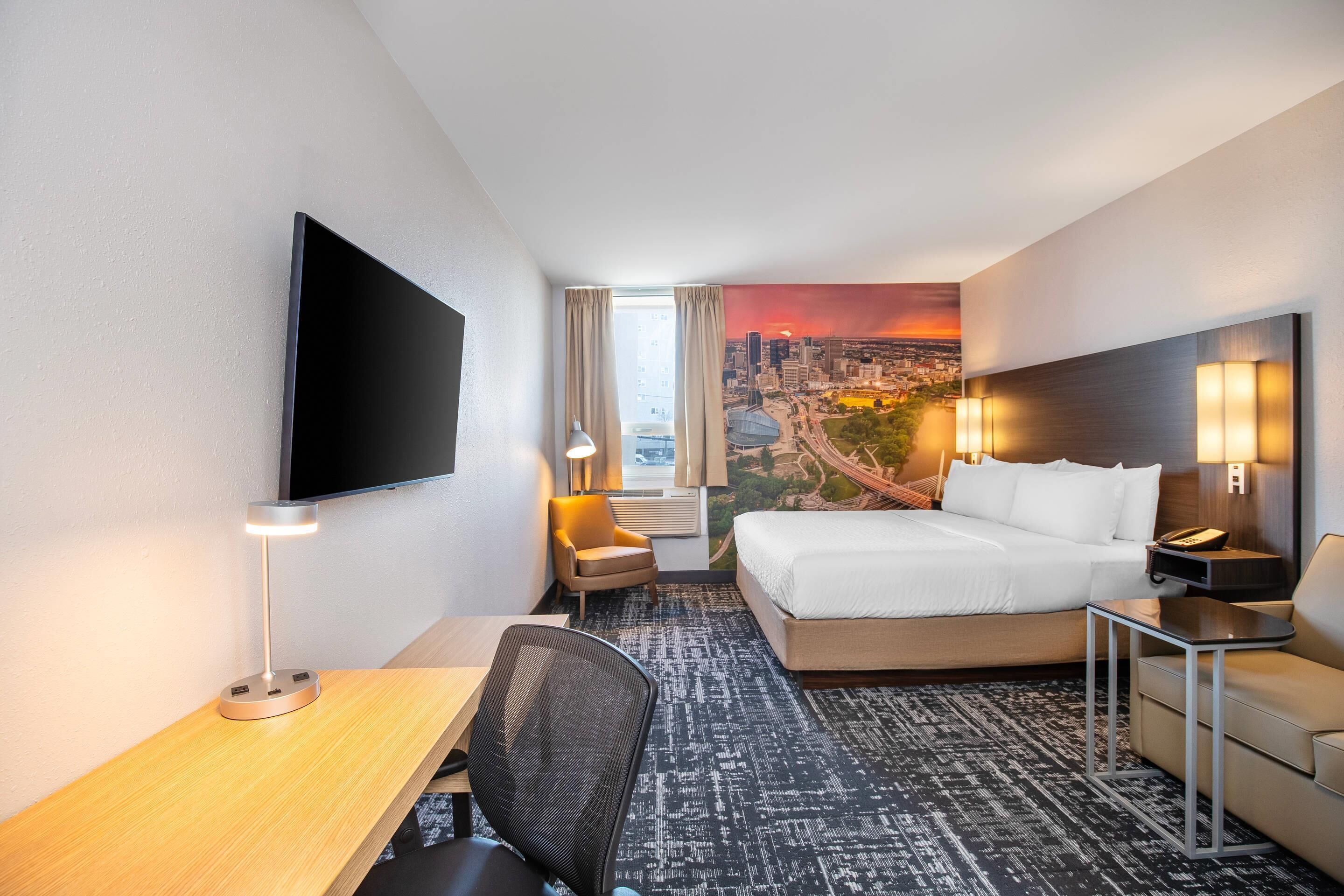 Habitación de hotel con cama, escritorio, silla, televisor y vista panorámica de la ciudad.
