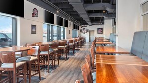 A restaurant with long wooden tables and chairs, large windows, and a high ceiling with exposed beams. - Clarion Pointe (Winnipeg)