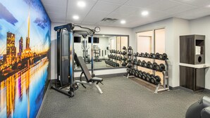 A gym with exercise equipment, a mirror, and a wall with a cityscape mural. - Clarion Pointe (Winnipeg)