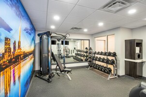 Un gimnasio con equipo de ejercicio, un espejo y una pared con un mural de un paisaje urbano.