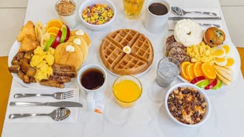 A breakfast spread with waffles, eggs, sausages, and various fruits on a table.