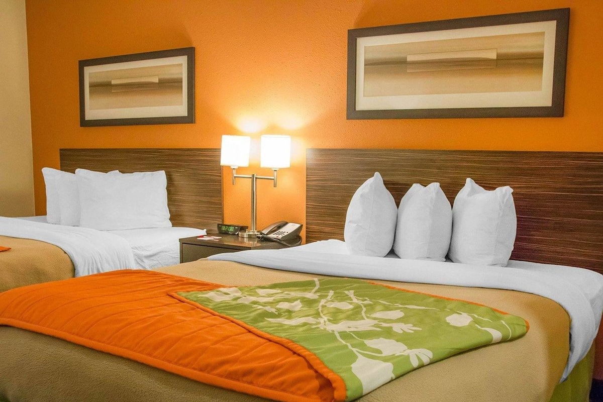 Una habitación de hotel con dos camas, una mesita de noche con lámpara y cuadros en la pared.