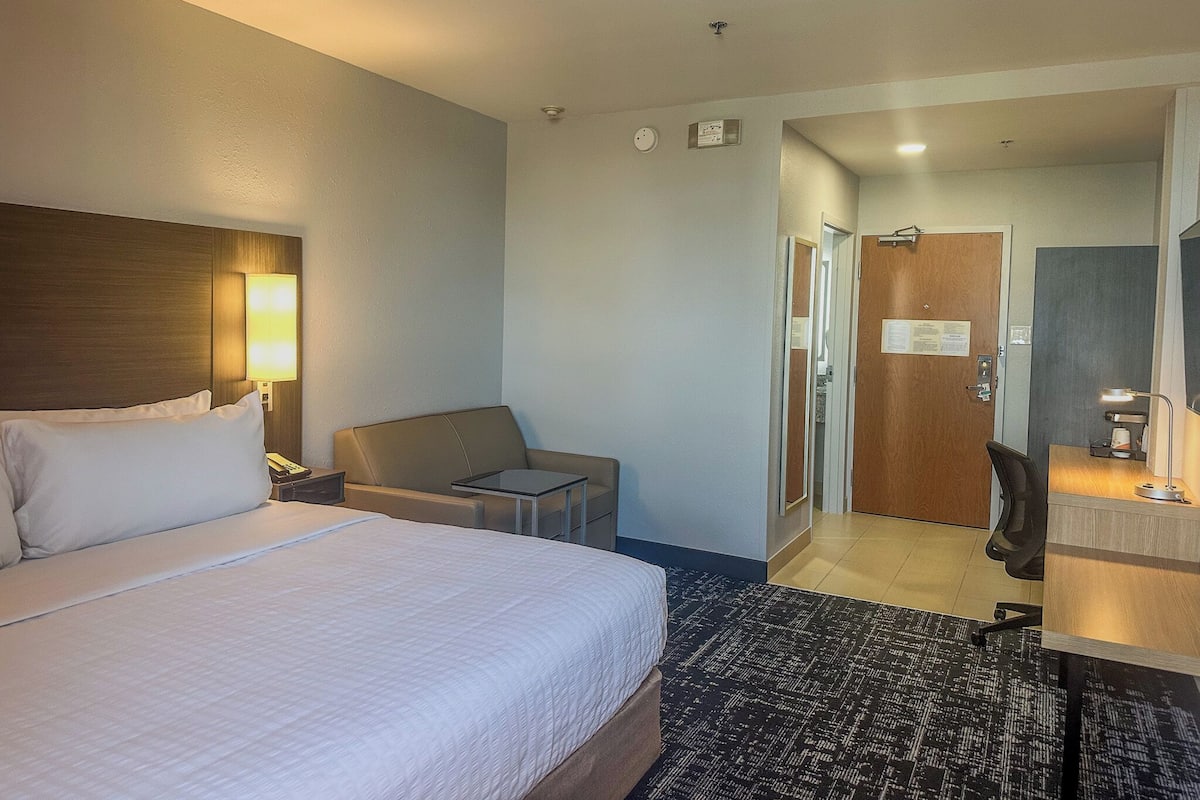 Une chambre d’hôtel comprenant un lit, un bureau, une chaise, une lampe et une porte donnant sur une salle de bain.