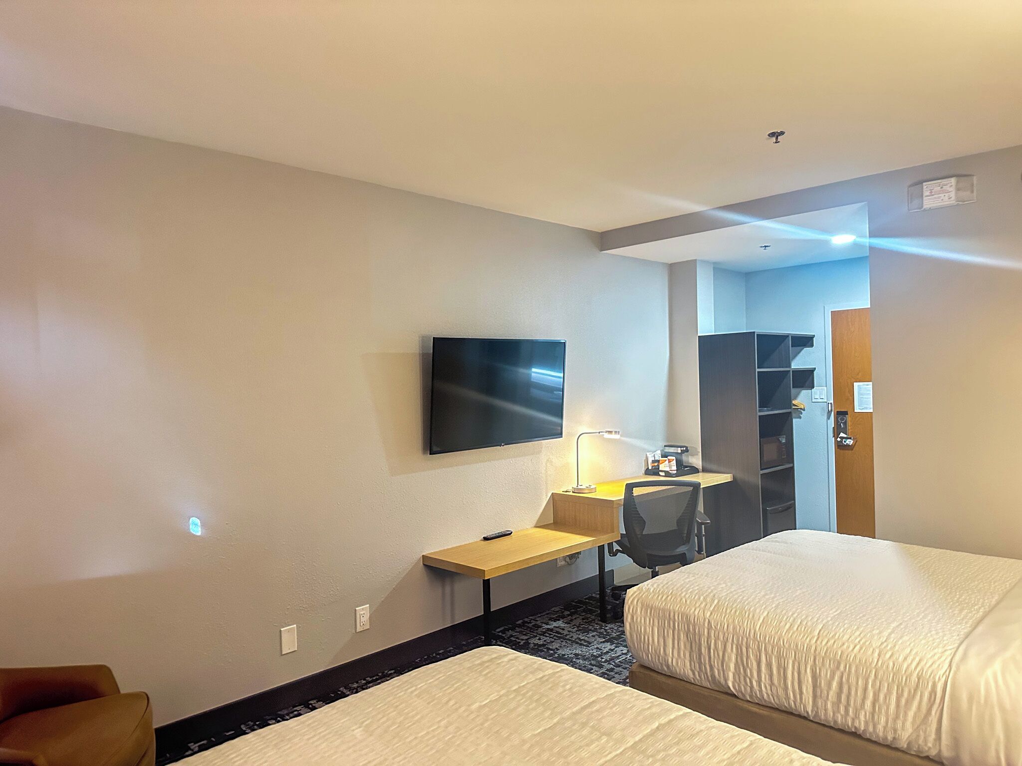 A hotel room with a bed, a desk with a chair, a TV mounted on the wall, and a door leading to a closet.