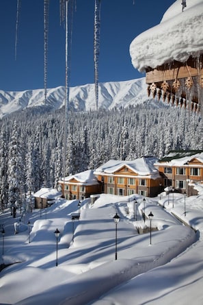 A snow-covered resort with wooden buildings, a ski slope, and a forested mountain backdrop. - The Khyber Himalayan Resort & Spa (Baramula)
