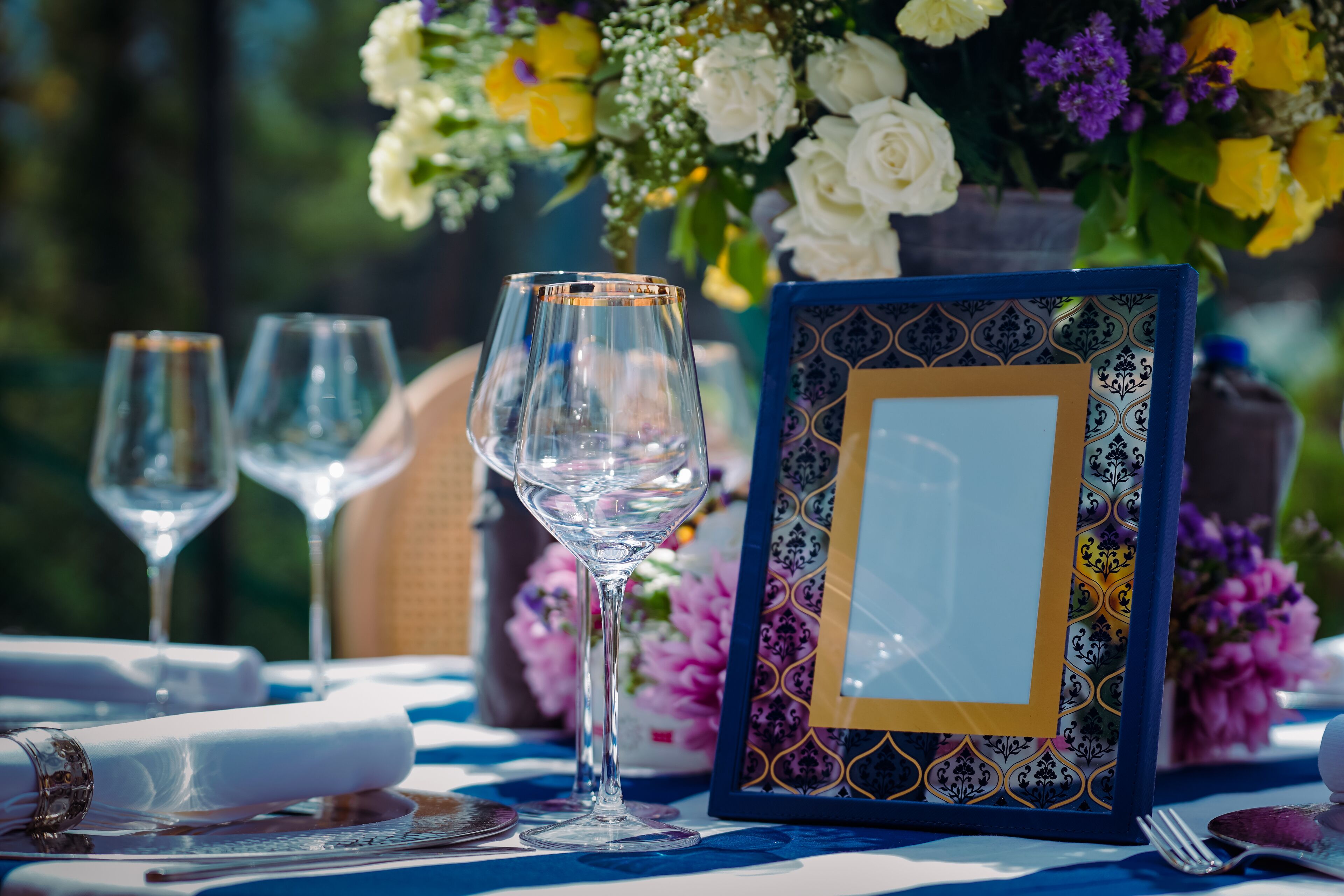 A table set with wine glasses, a framed picture, and a vase of flowers.