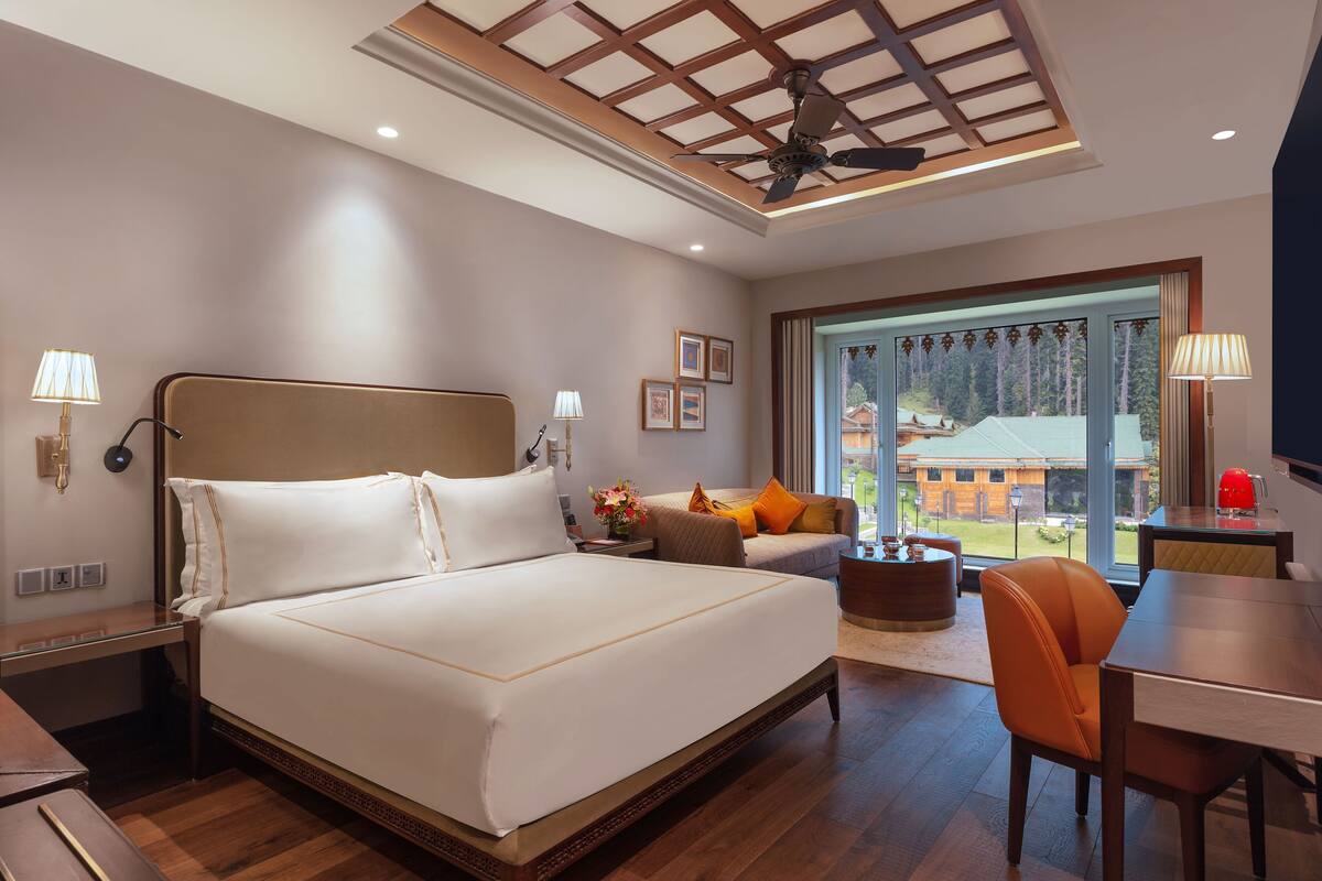 A modern hotel room with a large bed, a desk, a chair, and a view of the outdoors.