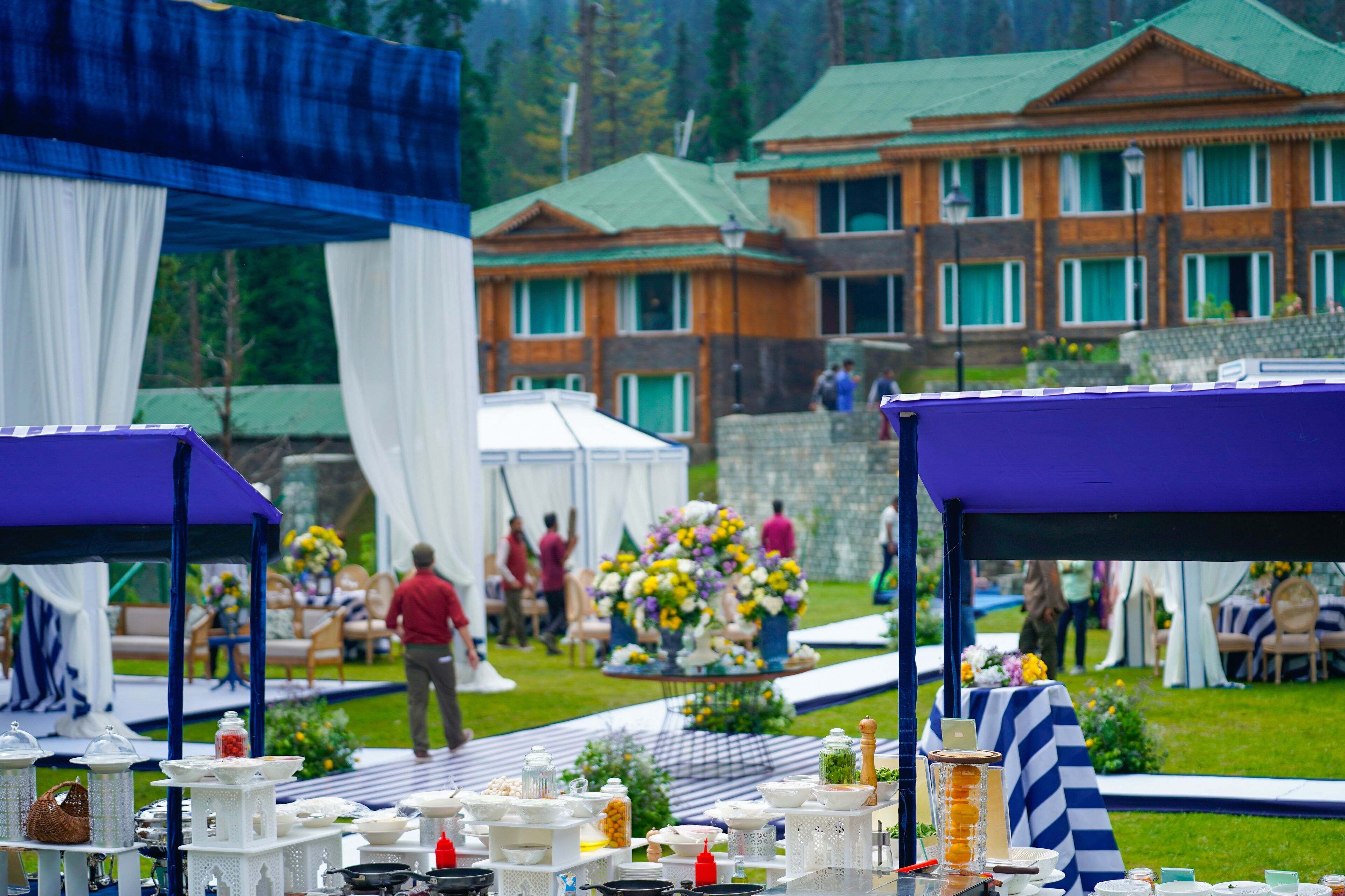 A tented outdoor event area with tables set up for dining, surrounded by a building with a green roof and multiple windows.