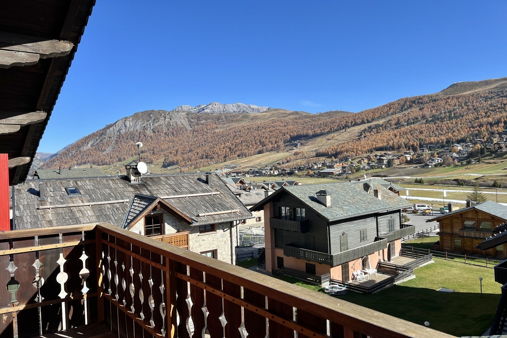 Un village de montagne aux maisons traditionnelles en bois, avec un ciel dégagé et une vue sur les montagnes lointaines.