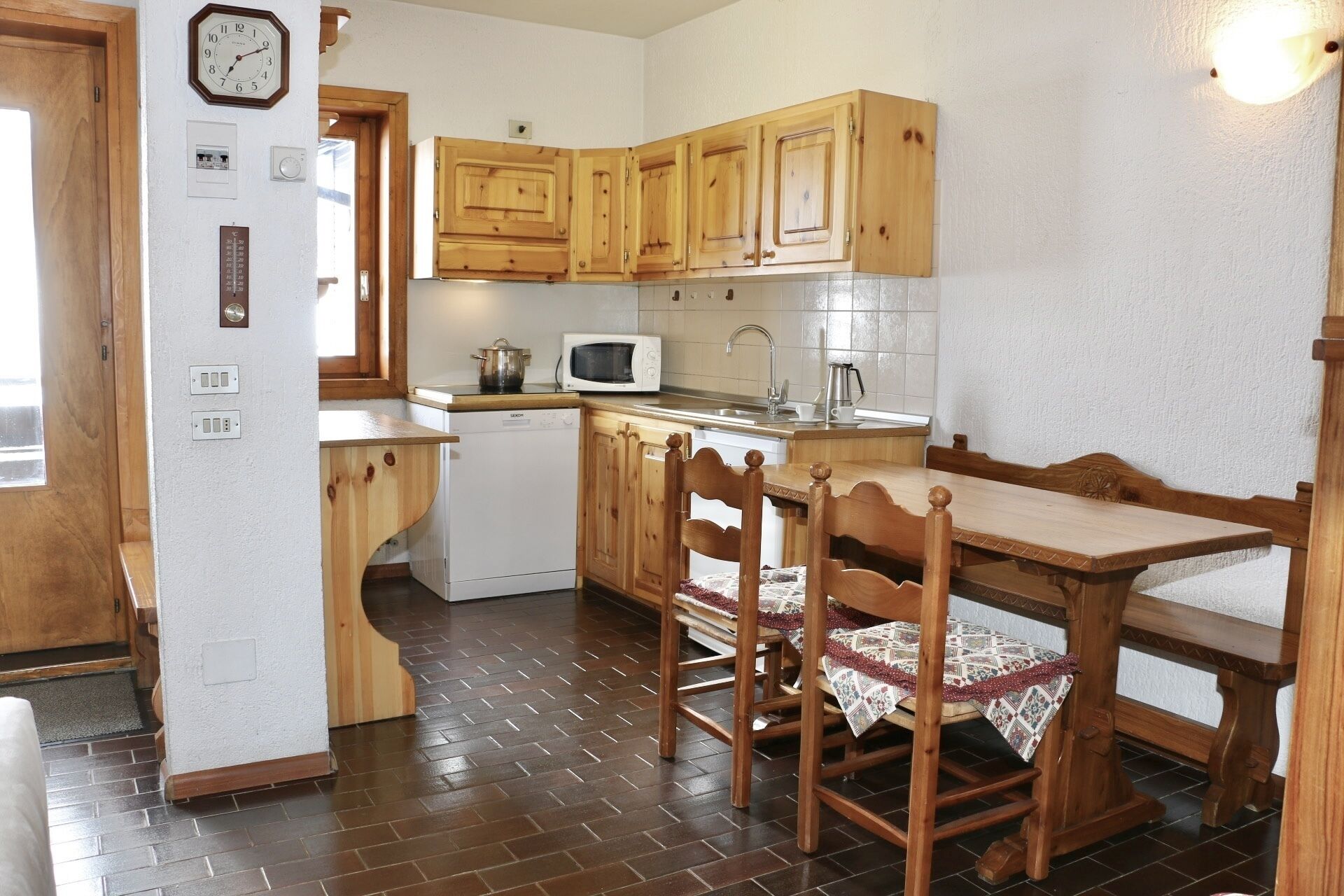 A kitchen with wooden cabinets, a microwave, a sink, and a dining table with chairs.