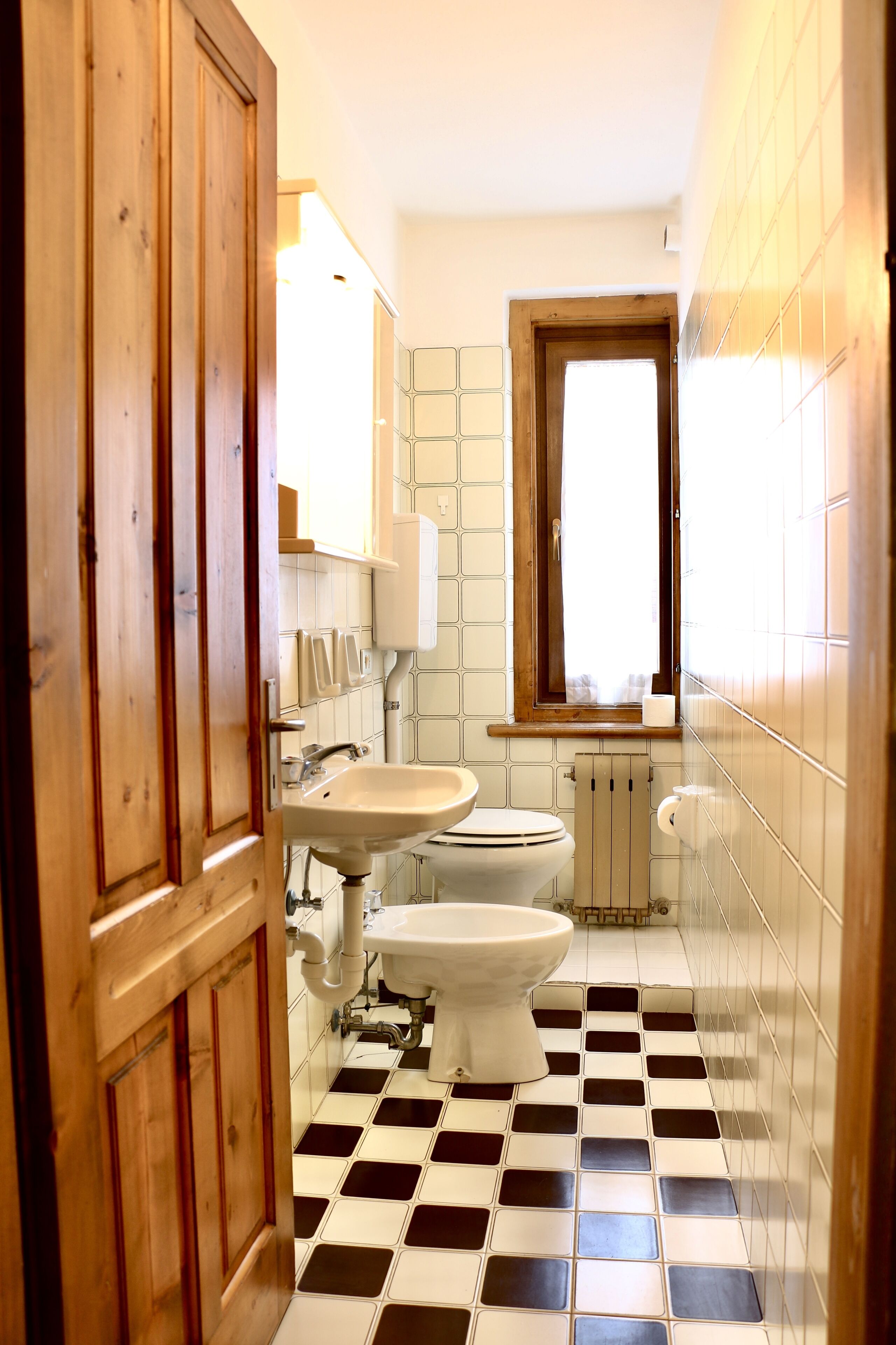 A bathroom with a checkered floor, a toilet, a sink, and a window.