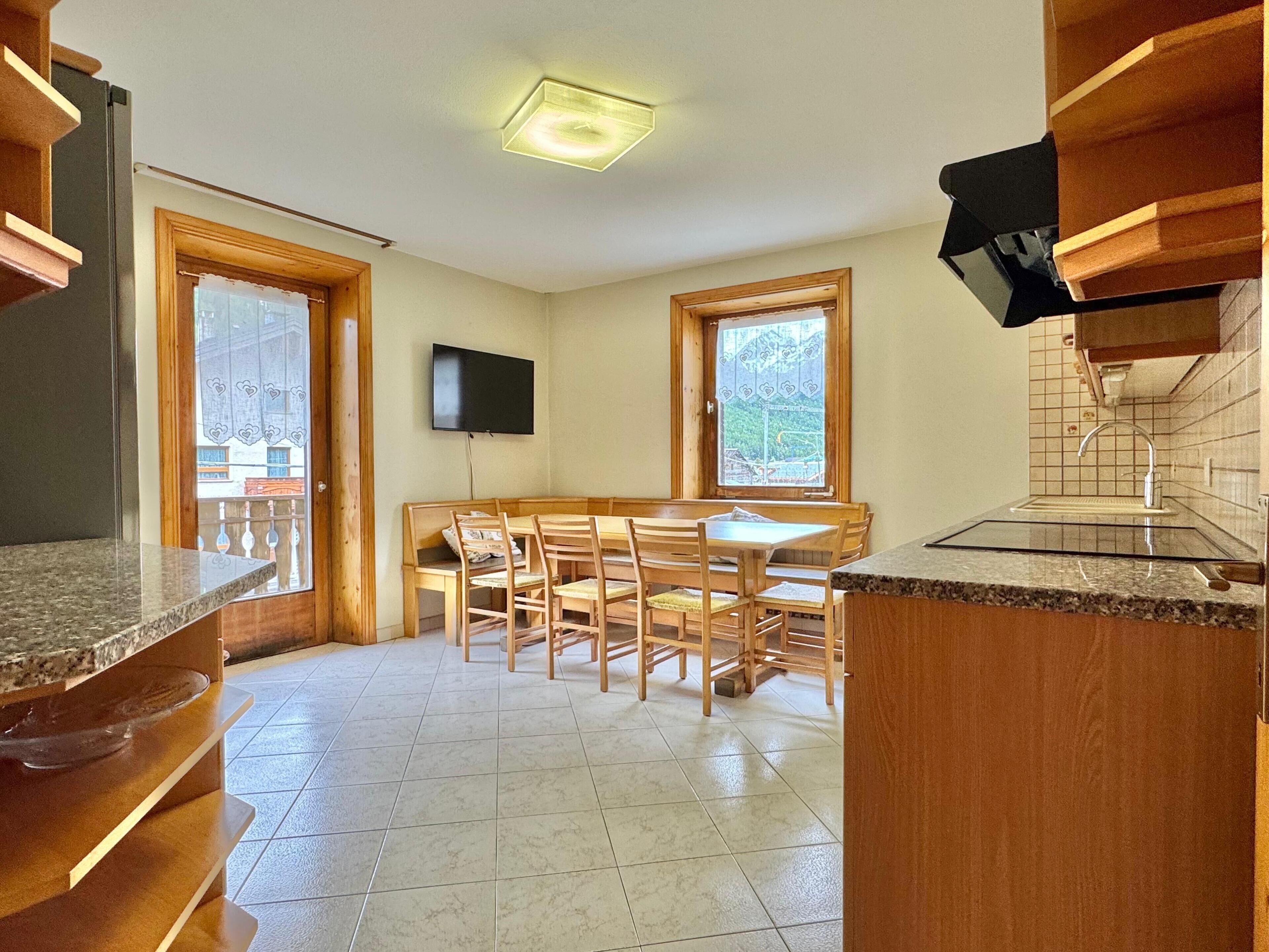 A kitchen with a dining area, wooden cabinets, a TV, and a window with a view.