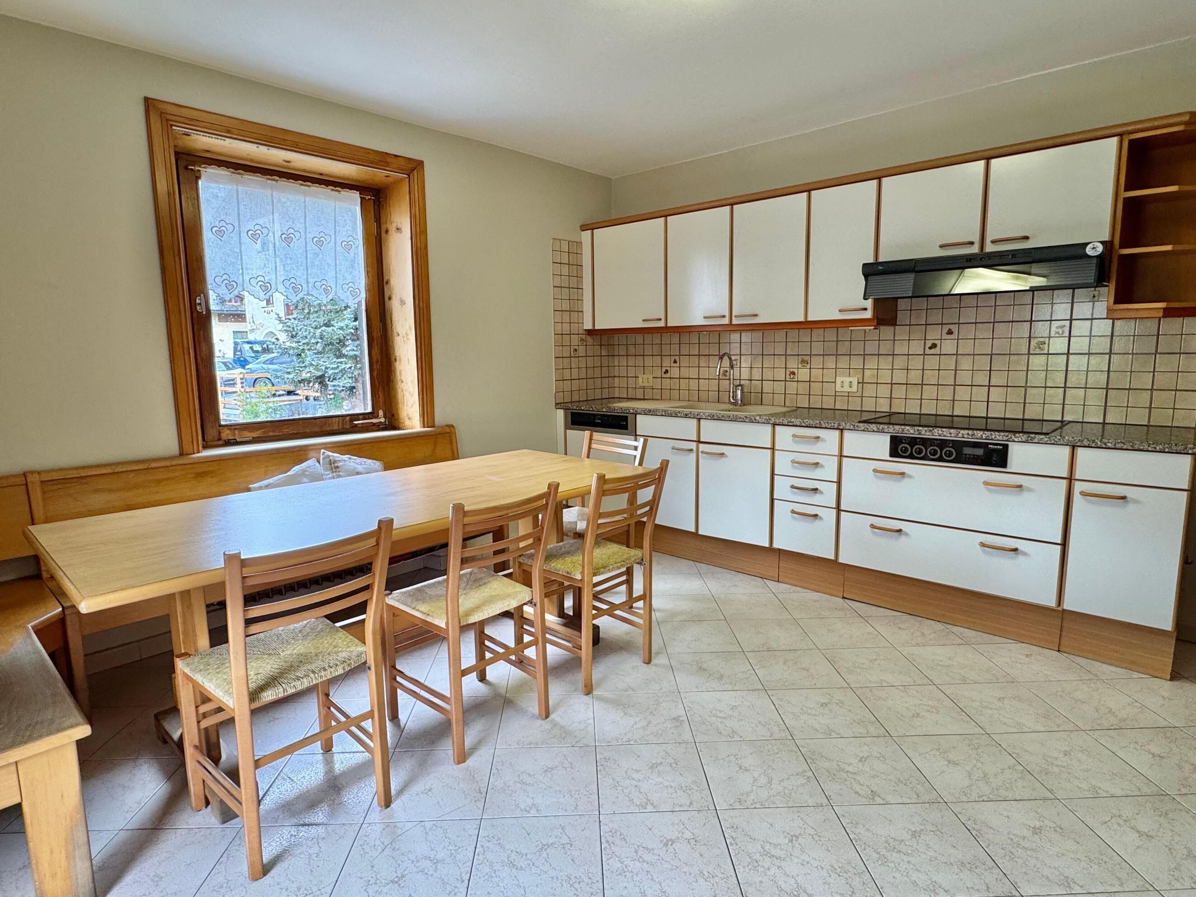 A kitchen with a wooden table and chairs, white cabinets, a tiled backsplash, and a window with a view of the outside.
