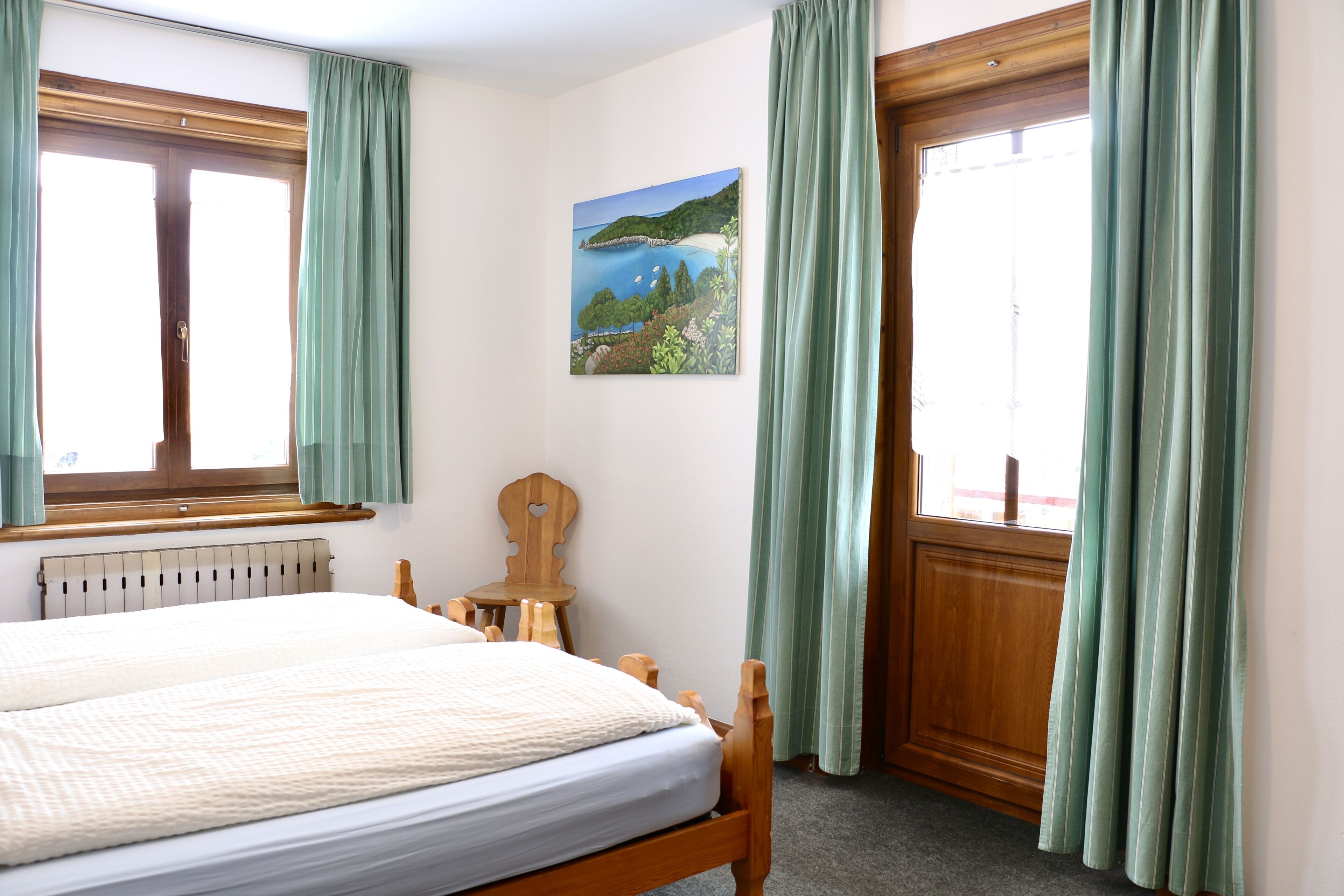 Camera da letto con un letto, una testiera in legno, un termosifone, un tavolino in legno e un dipinto di un paesaggio.