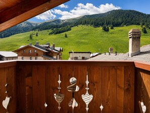 A wooden balcony with a view of a green hillside and buildings. - Roulette Apartments (Livigno)