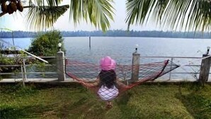 Niño con sombrero rosa y camisa a rayas de pie en una zona verde con vista a un lago y una cerca.