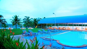Una piscina con sillas de descanso, un área de estar cubierta y palmeras.