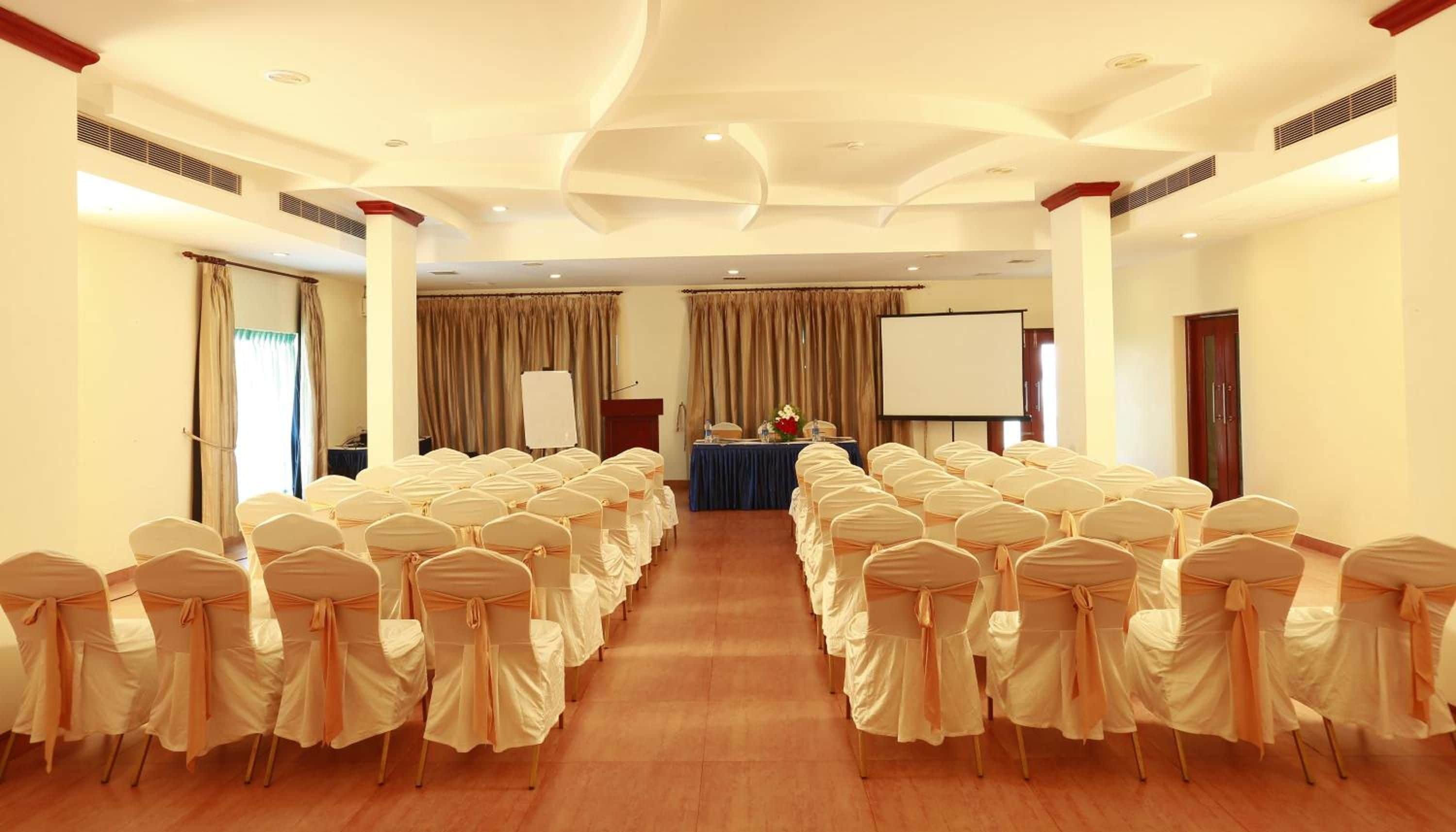A conference room with rows of chairs, a podium, and a projection screen.