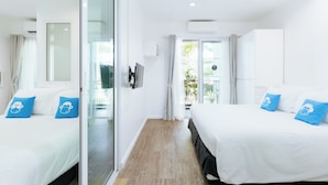 A modern hotel room with two beds, a sliding glass door leading to a balcony, and a flat-screen TV on the wall. - Blu Monkey Bed & Breakfast Phuket (Phuket)