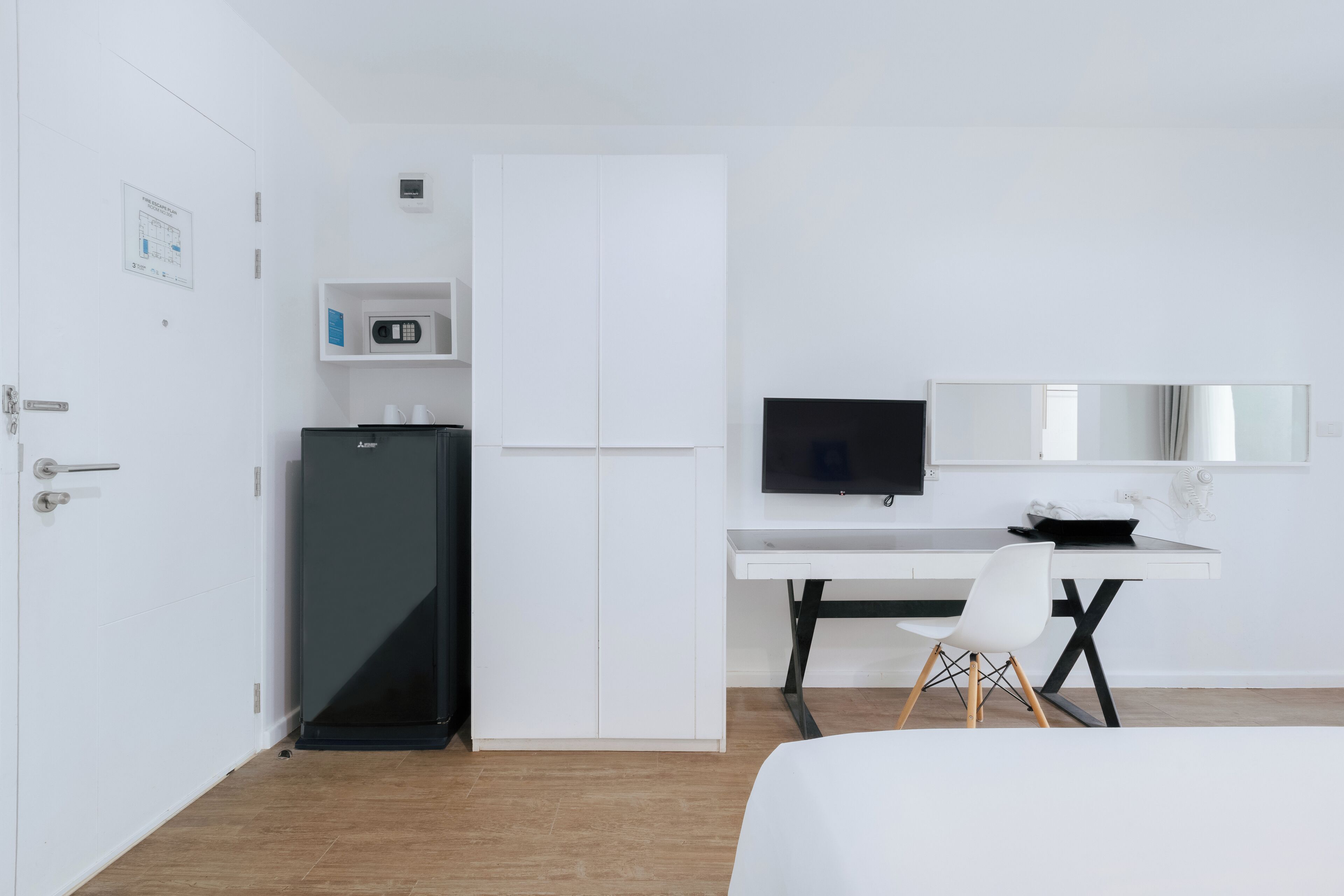 A modern hotel room with a bed, a desk with a computer, a television, and a refrigerator.